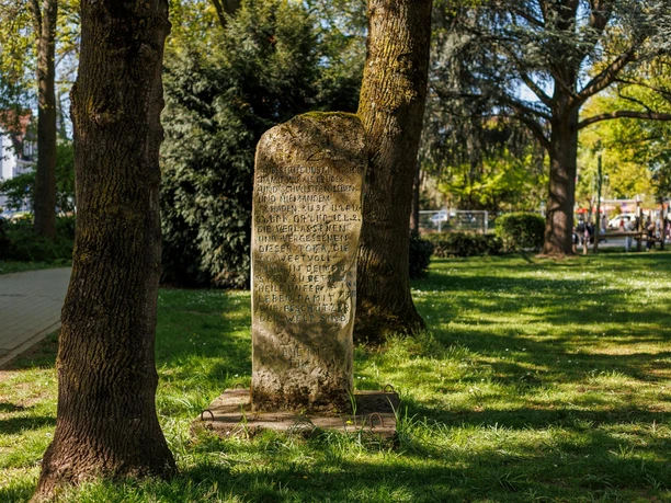 Sprechender Stein mit Inschrift zwischen Bäumen auf einer sonnigen Grünfläche in Leichlingen