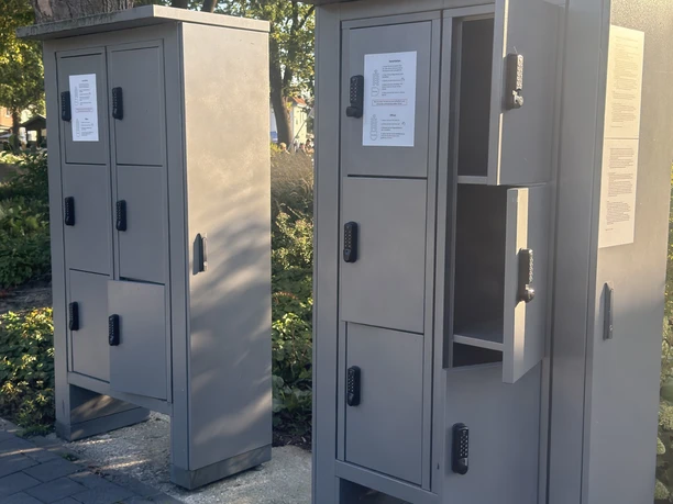 Graue Schließfächer mit Zahlenschlössern unter Bäumen am Strandterrassenplatz.