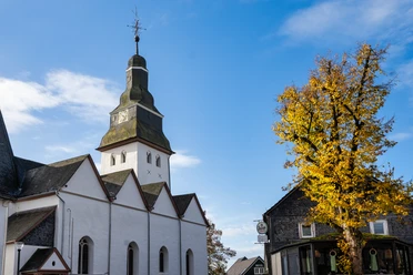 Dorfkirche in Nümbrecht mit Turm, Herbstbaum und blauem Himmel