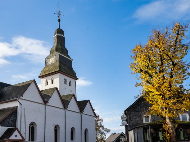 1000-jährige Dorfkirche Dorfkirche in Nümbrecht mit Turm, Herbstbaum und blauem Himmel