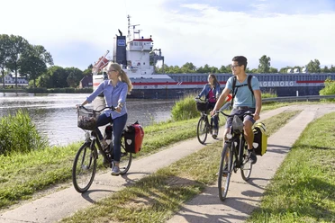 Radtour Große Pötte Radfahrer am Kanal neben vorbeifahrendem Schiff