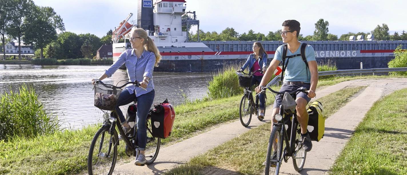 Radtour Große Pötte Radfahrer am Kanal neben vorbeifahrendem Schiff