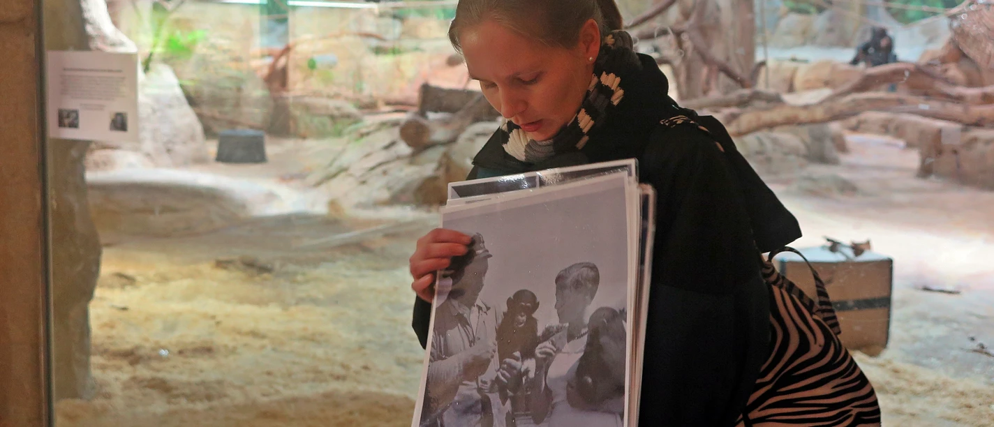 Zooführerin hält historische Fotos vor einem Tiergehege im Zoo am Meer.