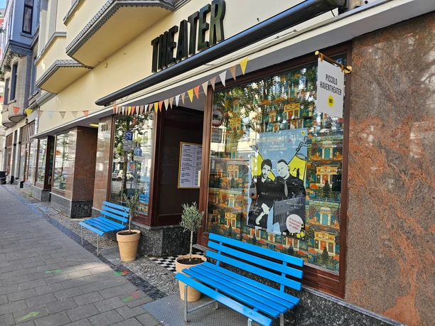 Eingang des Piccolo Haventheaters mit Schaufenster, Plakat und blauen Bänken.