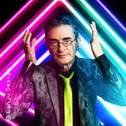 Mathias Richling mit Brille vor bunten Neonlinien, die Hände seitlich erhoben