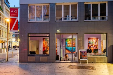 Abendliche Außenansicht der Art Galerie 7 in Köln mit beleuchteten Schaufenstern.