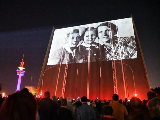 Publikum vor nächtlicher Fassadenprojektion mit historischem Porträt und Turm.