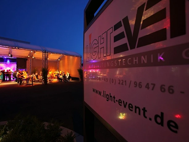 An illuminated event tent at night with a "Light Event" sign in the foreground