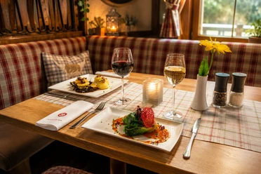 Sauerländer Hof Gedeckter Tisch Festlich gedeckter Holztisch im Sauerländer Hof mit regionalen Speisen, Rot- und Weißwein, Kerze und gelber Blume.