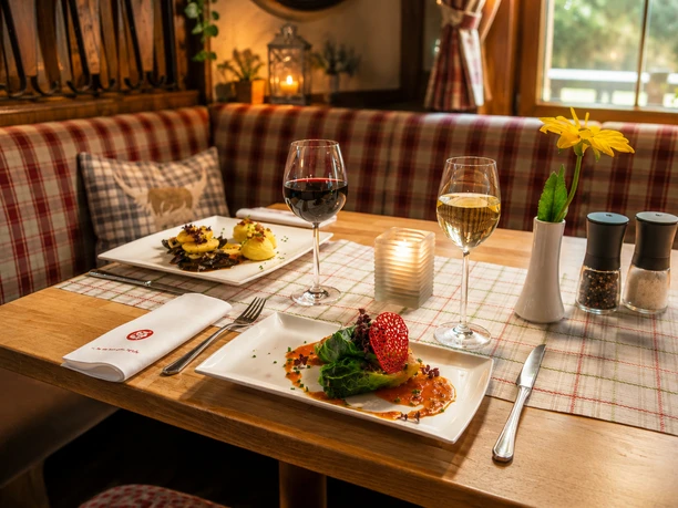 Sauerländer Hof Gedeckter Tisch Festlich gedeckter Holztisch im Sauerländer Hof mit regionalen Speisen, Rot- und Weißwein, Kerze und gelber Blume.