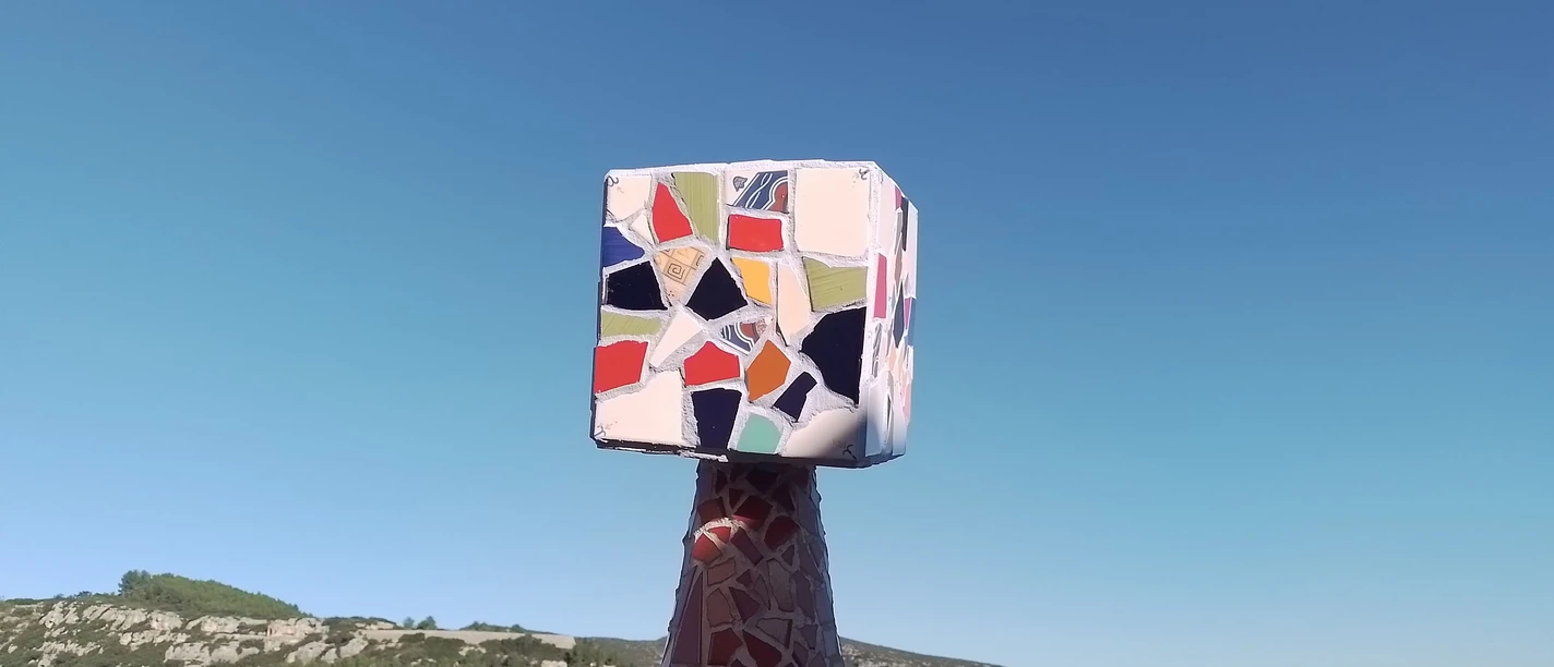 Mosaikskulptur mit buntem Würfelkopf vor blauem Himmel und weiter Landschaft