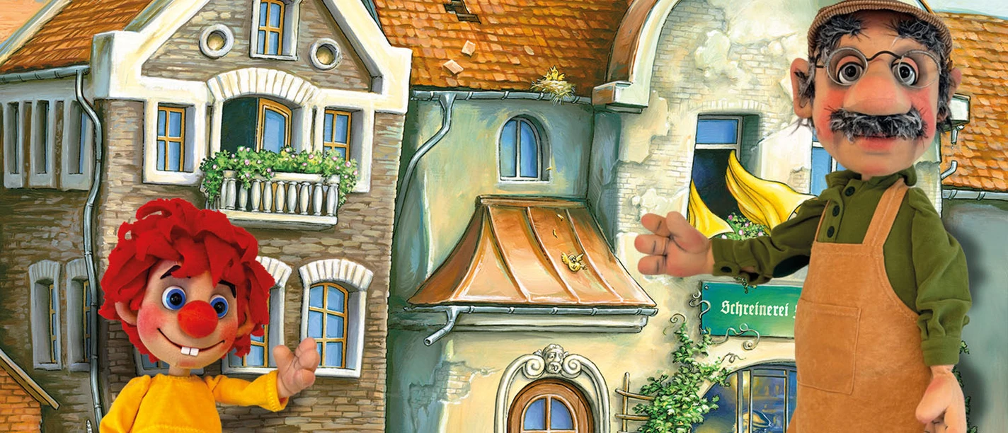 Pumuckl und Meister Eder als Figuren vor einer bemalten Häuserkulisse