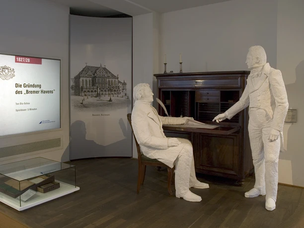 Museumsszene zur Gründung Bremerhavens mit Figuren, Schreibtisch und Vitrine.