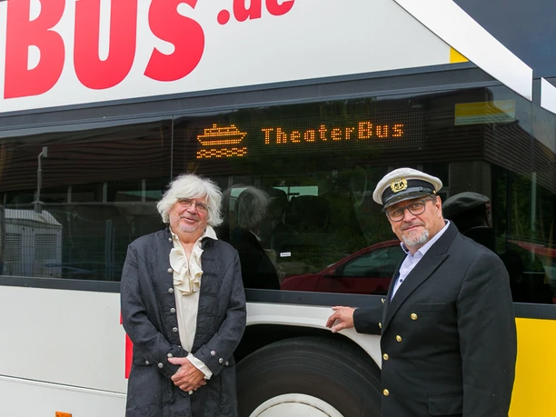 Zwei kostümierte Männer vor einem Bus mit Anzeige „TheaterBus“.