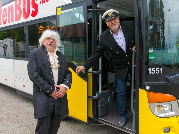 Zwei Männer in historischen Kostümen stehen an der geöffneten Tür eines HafenBusses.