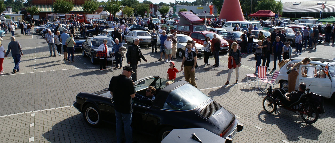 Oldtimertreffen mit vielen Besuchern und klassischen Autos auf einem Parkplatz.