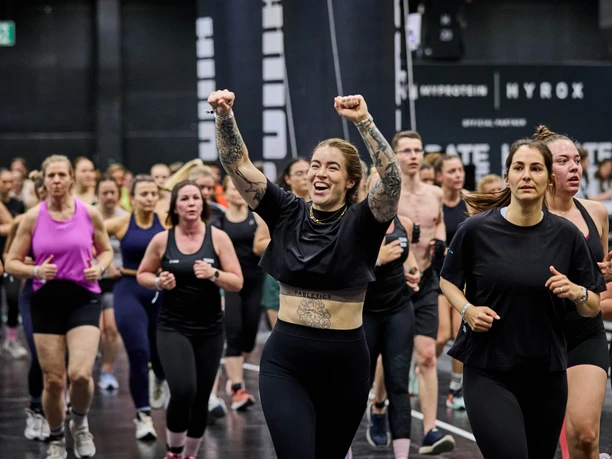 FIBO in Köln Teilnehmende laufen bei der FIBO in einer Messehalle, vorn jubelt eine Sportlerin.