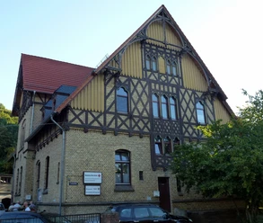 Ein großes Fachwerkhaus mit gelben Backsteinwänden, dunklen Holzbalken und einem roten Ziegeldach.