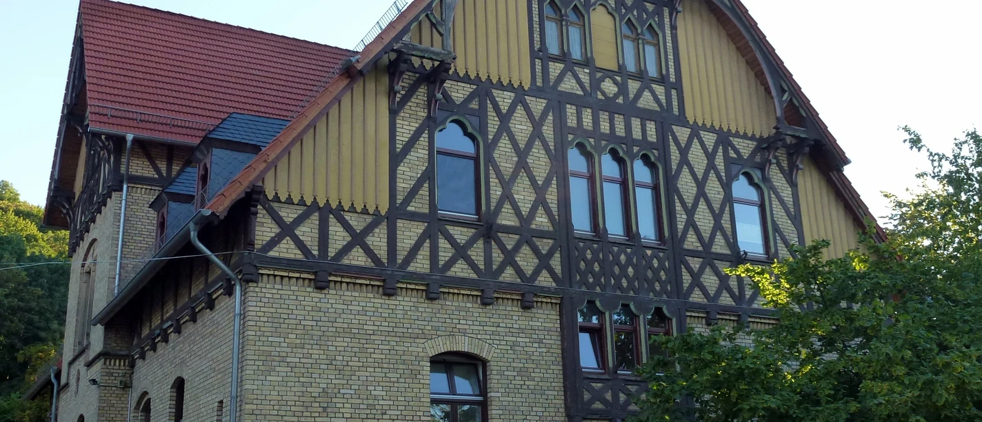 Ein großes Fachwerkhaus mit gelben Backsteinwänden, dunklen Holzbalken und einem roten Ziegeldach.