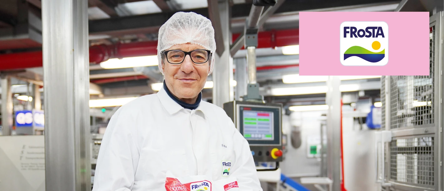Mann in Schutzkleidung hält eine FRoSTA-Packung in der Produktionshalle.