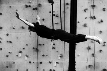 AHK Artistik Schwarz-Weiß-Aufnahme einer Artistin am Vertikaltuch vor einer Kletterwand
