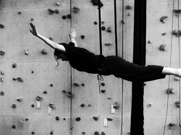 AHK Artistik Schwarz-Weiß-Aufnahme einer Artistin am Vertikaltuch vor einer Kletterwand