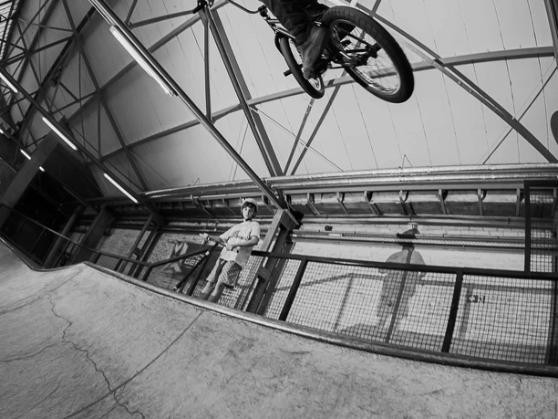 AHK BMX and Skate Ramp A BMX rider, dressed in black and white, leaps high over the ramp at the Abenteuerhallen Kalk