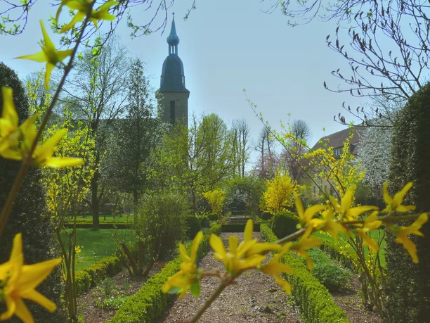 Hufeisen-Route im Osnabrücker Land Church steeple towers over flowering spring bushes in a sunny garden.