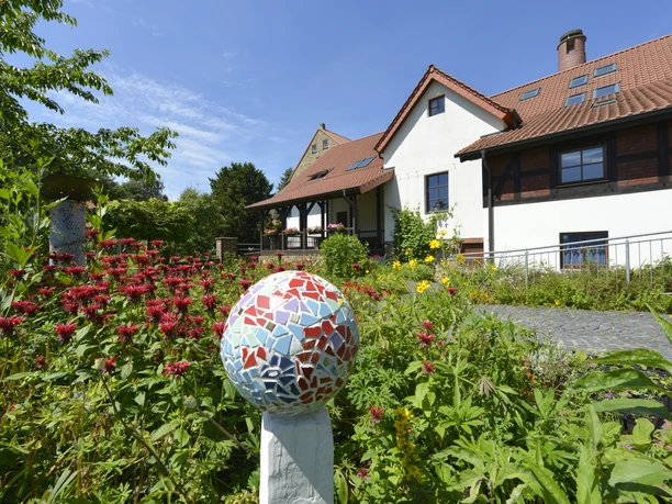 Hufeisen-Route im Osnabrücker Land Multicolored mosaic on a pole in a colorful flowering garden in front of a house with wooden half-timbering.