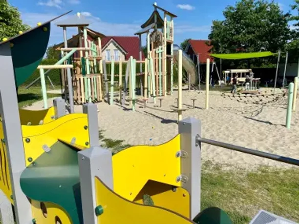 Kinderspielplatz Frickenhake mit gelben Spielgeräten, Kletterturm und Rutsche auf Sandboden.