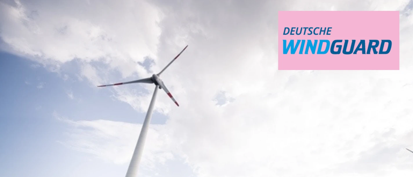 Windenergieanlage hinter Gebäuden der Deutschen WindGuard, oben rechts das Firmenlogo.