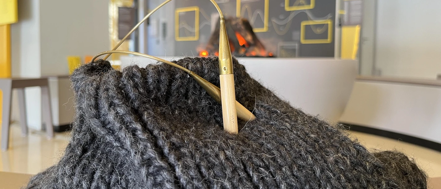 Strickteil aus grauer Wolle, in dem Nadeln stecken