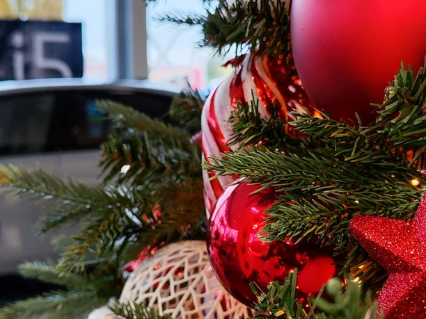 Rote Weihnachtskugeln, Stern und Tannenzweige vor einem Auto im Autohaus.