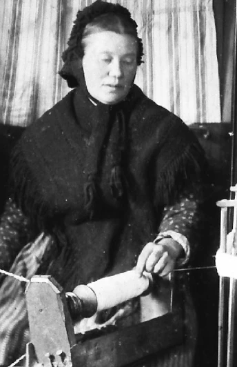 Eine Frau spinnt Leinen an einem alten Spinnrad, umgeben von traditionellen Webutensilien.