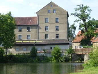 Die historische Brausemühle mit ihrem rotgedeckten Dach steht malerisch am Ufer eines ruhigen Teichs.