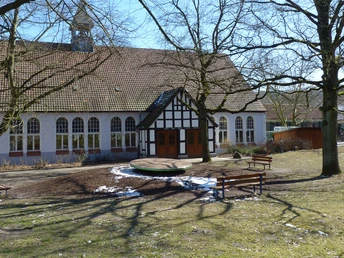 Fachwerkgebäude der evangelischen Jugendhilfe Schweicheln, umgeben von Bäumen und Sitzplätzen.