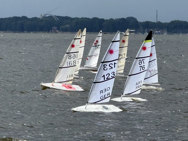 Mehrere RC-Laser-Segelboote mit weißen Segeln auf bewegtem Wasser.