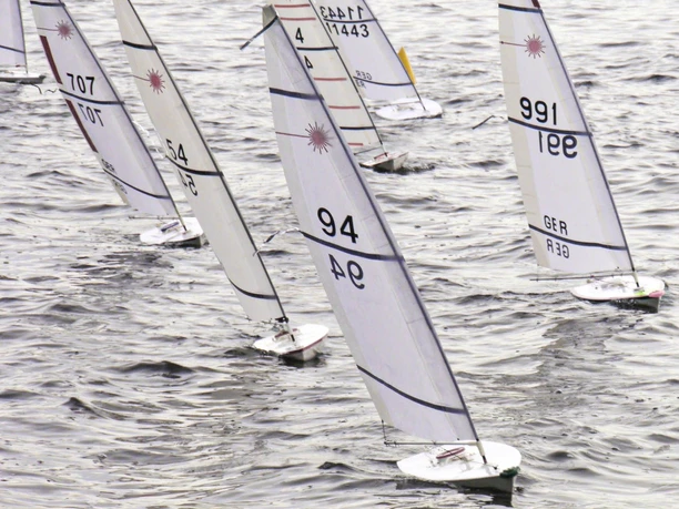 Mehrere RC-Laser-Segelboote mit weißen Segeln auf bewegtem Wasser.