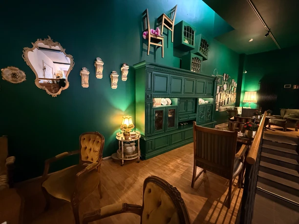 Café Wunderland Grüner Gastraum des Café Wunderland mit antiken Sesseln und surrealer Wanddekoration.