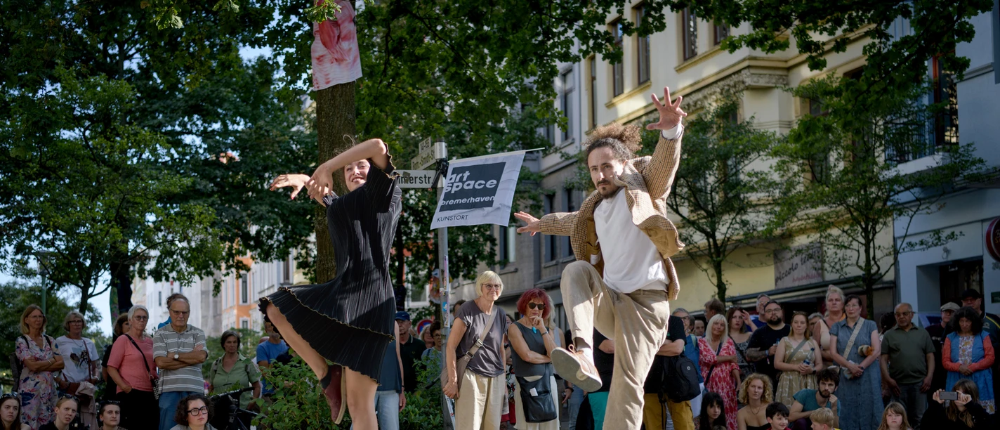 Zwei Tänzer springen bei einer Open-Air-Performance vor Publikum in Bremerhaven.