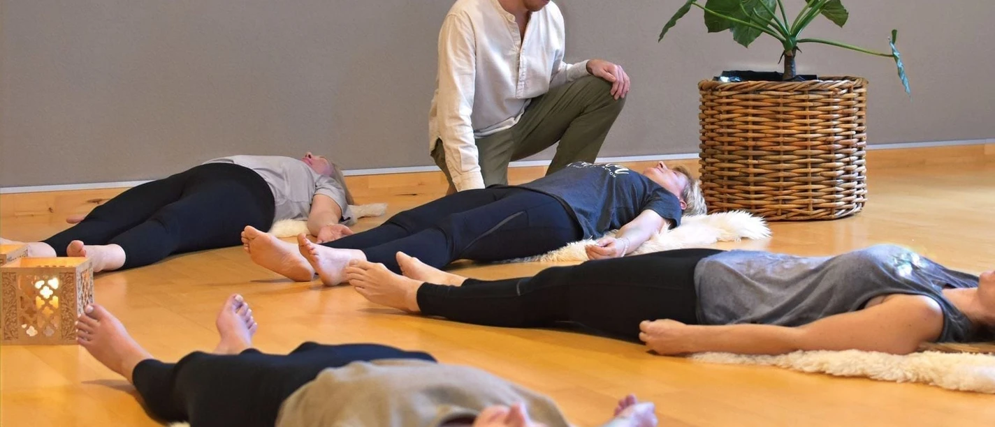 Teilnehmende liegen entspannt. Ein Kursleiter begleitet sie bei einer Breathwork-Session.