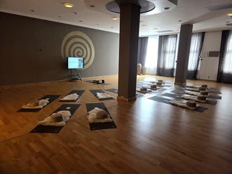 Großer Raum im yogawirkt mit Matten, Fellen und Kissen, an der Wand eine goldene Spirale
