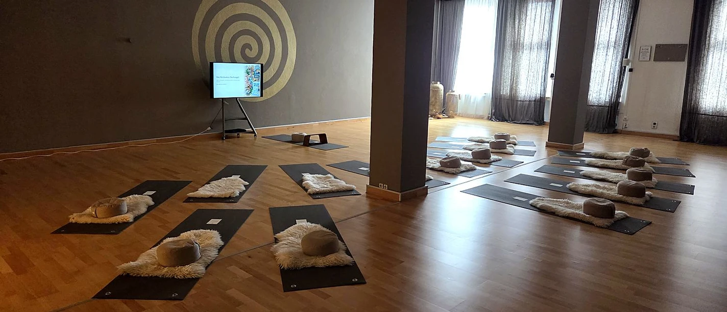 Großer Raum im yogawirkt mit Matten, Fellen und Kissen, an der Wand eine goldene Spirale