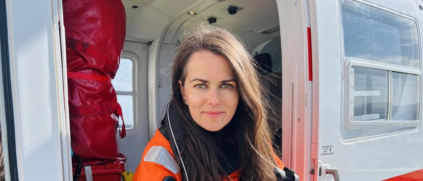 Fotografin Esther Horvath in orangefarbener Schutzkleidung mit Kamera im Hubschrauber.