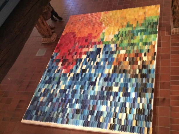 Farbiges Wachsschiffchen-Mosaik auf rotem Fliesenboden unter Holzbalken.