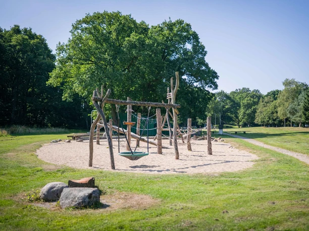 Naturnaher Spielplatz mit Holzgerüsten im Grünen unter blauem Himmel.