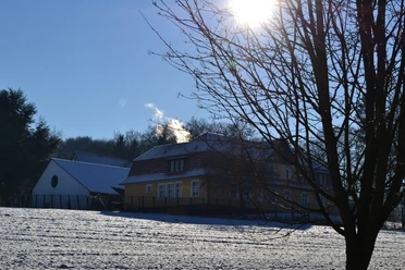 Ev. Stiftung Ummeln, ehemalige Waldheimat Winterliche Landschaft mit einem schneebedeckten Haus, kahlen Bäumen und strahlender Sonne.