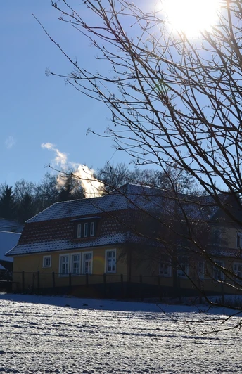 Ev. Stiftung Ummeln, ehemalige Waldheimat Winterliche Landschaft mit einem schneebedeckten Haus, kahlen Bäumen und strahlender Sonne.