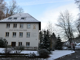 Einrichtung Waldheimat - Haus Morgensonne Schneebedecktes Gebäude "Haus Morgensonne" mit Bäumen im Hintergrund und verschneiter Umgebung.