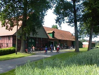 Eine Gruppe von Radfahrern vor einem großen roten Backsteingebäude in einer grünen Landschaft.